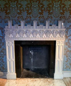 A fireplace in Strawberry Hill House - it is square and white with blue and gold patterned wallpaper on the wall behind