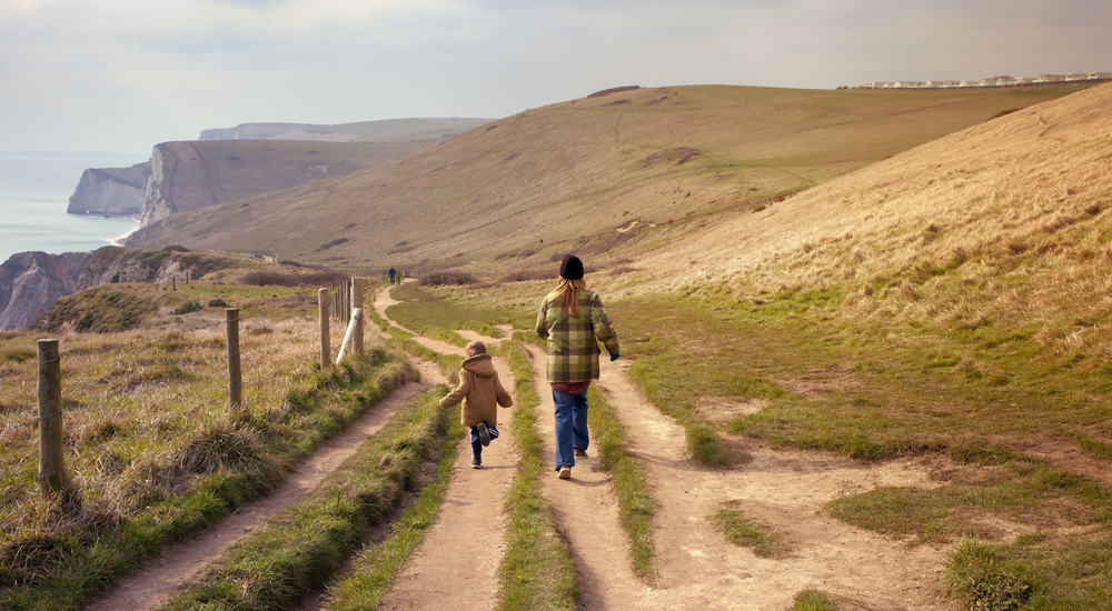 An adult and child walking along the top of coastal cliffs in Dorset