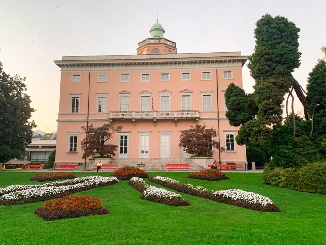 Villa Ciani, a lovely pink coloured building with a lawn and flower beds in front of it