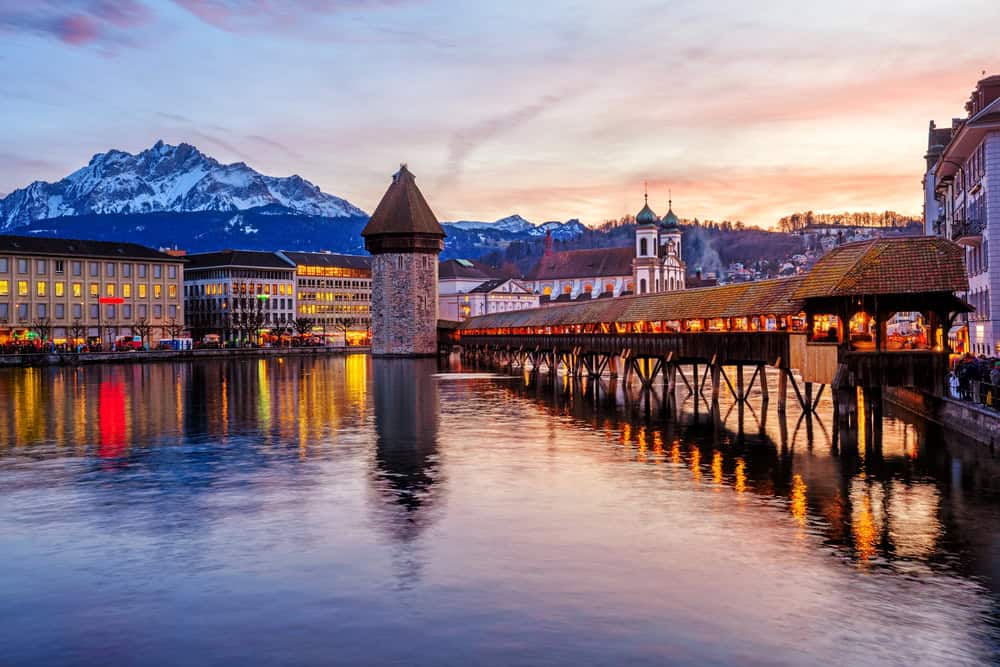 A view of Lucerne, at sunset, including part of the lake and bridge, with mountains in the background