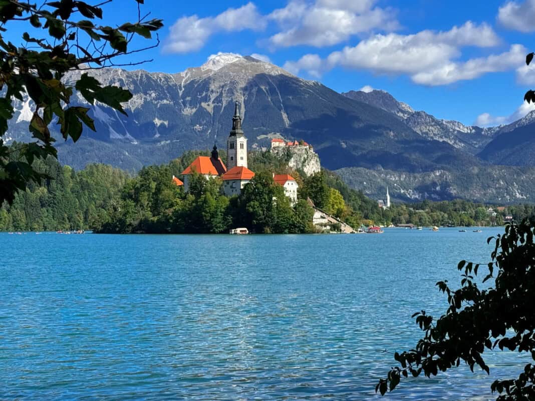 A view of the island in Lake Bled though a gap in the trees. Mountains are in the background.
