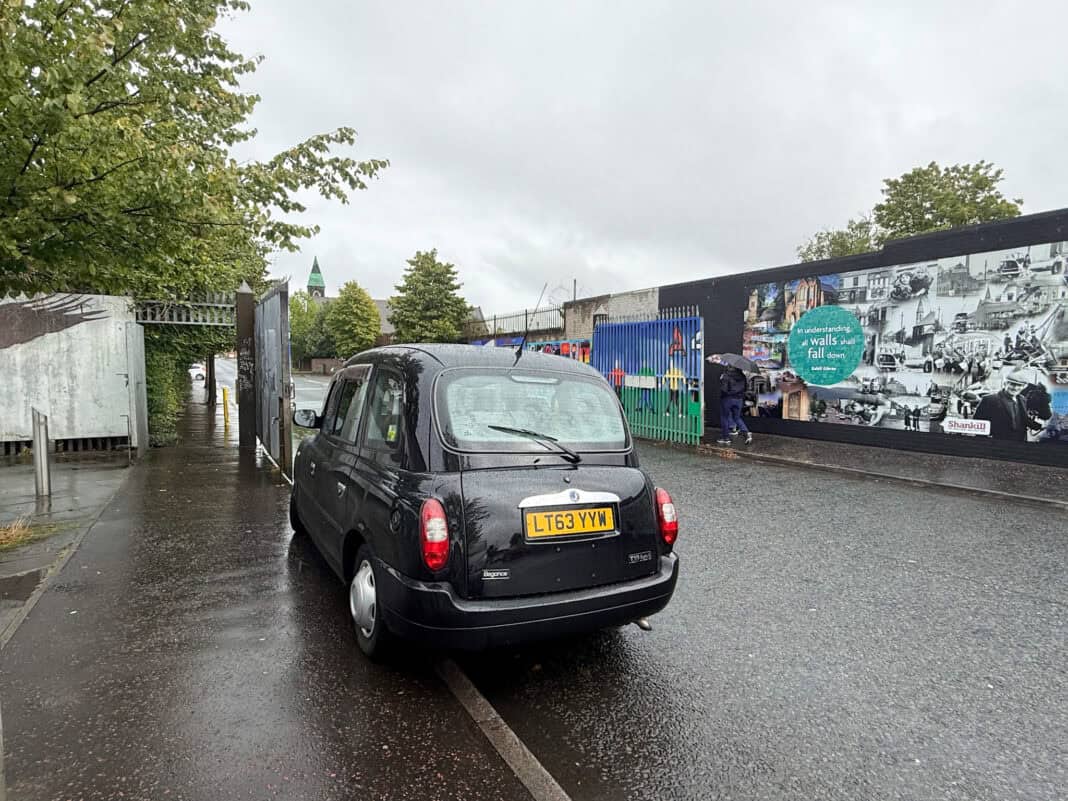 A black taxi by one of the wall murals on a tour in Belfast