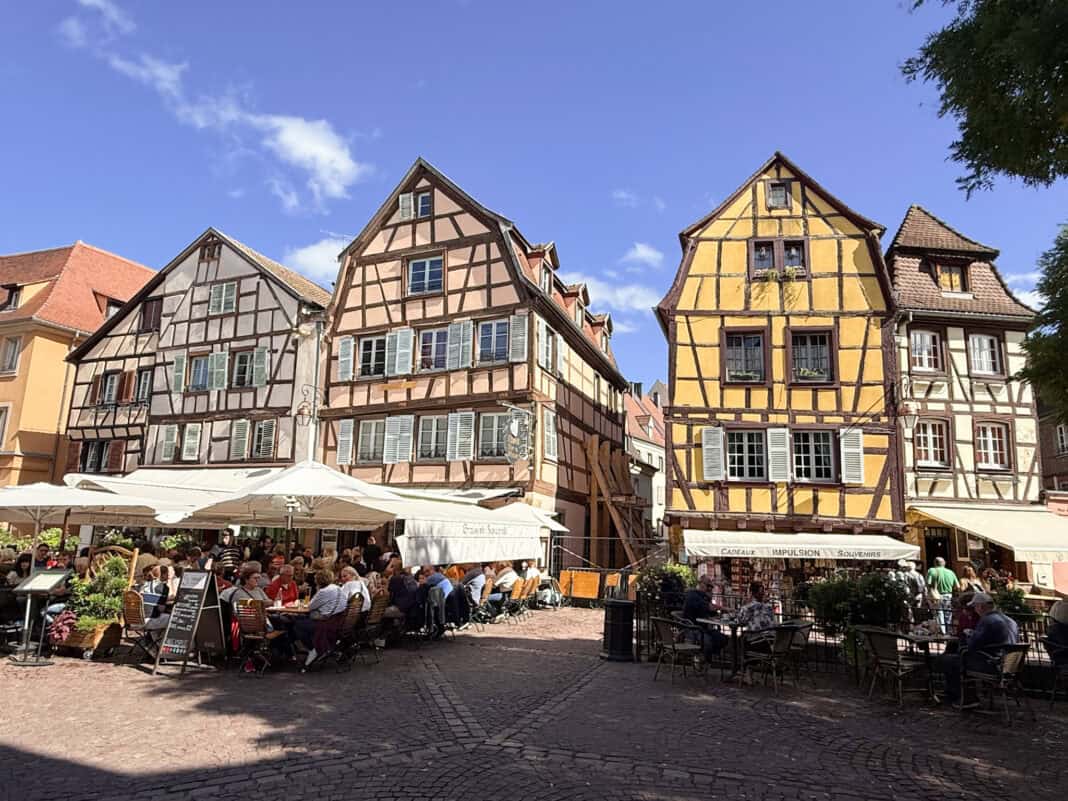 Some colourful half timbered houses around a square in Colmar with cafe and restaurants with outdoor seating